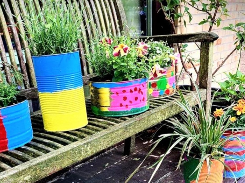 Blumen in bunt bemalten Blumentöpfen, die auf einer Holzbank stehen