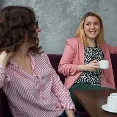 zwei Frauen sitzen nebeneinander, reden und haben Kaffeetassen vor sich auf dem Tisch stehen