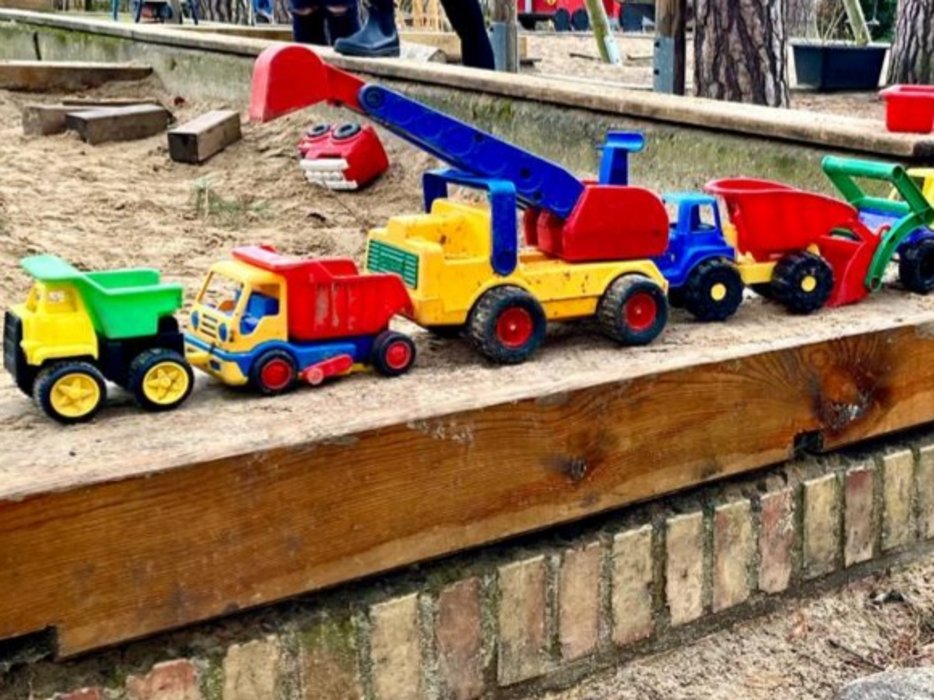 mehrere bunte Spielzeugautos die auf dem Rand des Sandkastens stehen
