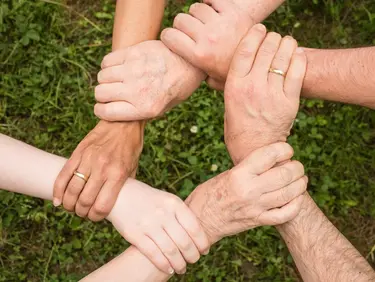 mehrere Hände halten sich an den Handgelenken und formen einen Kreis