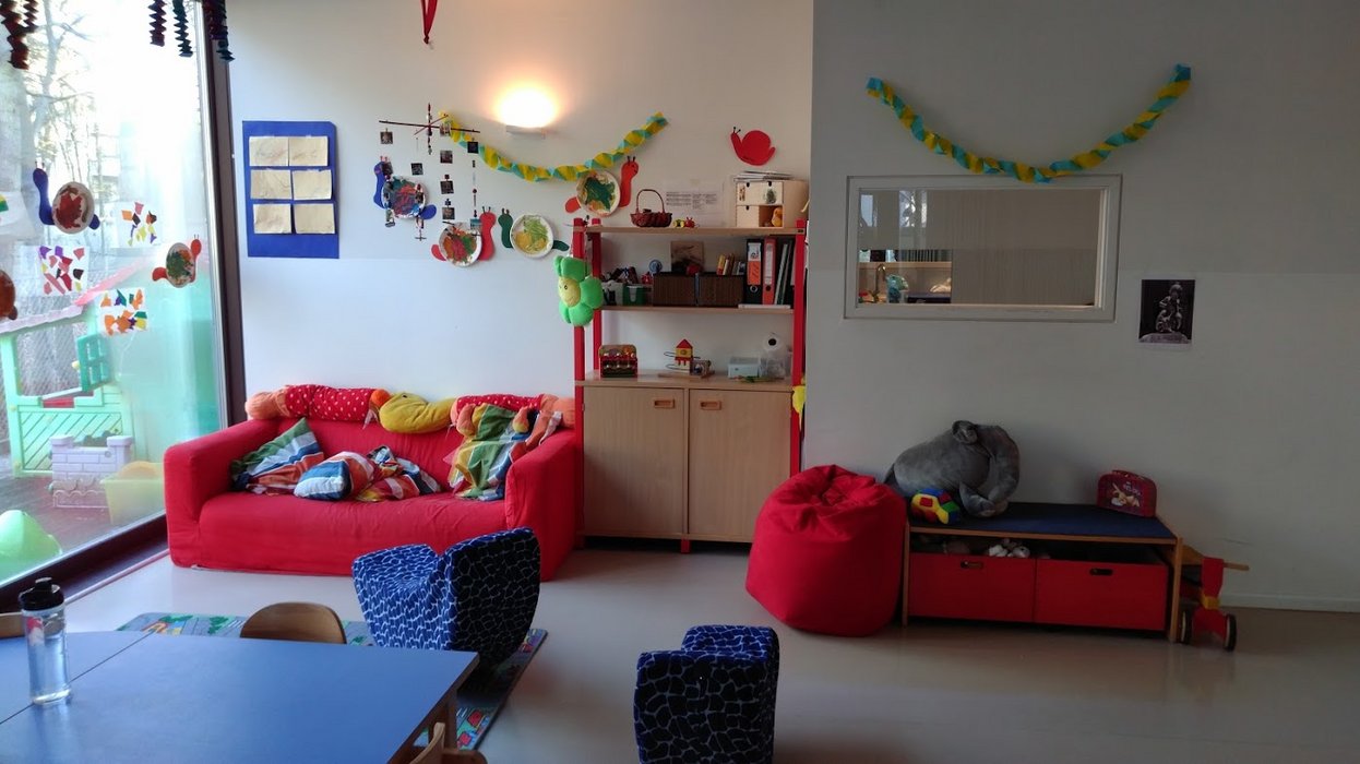 Der Raum der Krippenkinder im Kindergarten mit Regalen, einem roten Sofa und Spielsachen