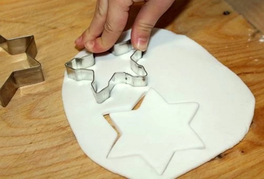 eine Hand, die mit sternförmigen Ausstechern Teig aussticht