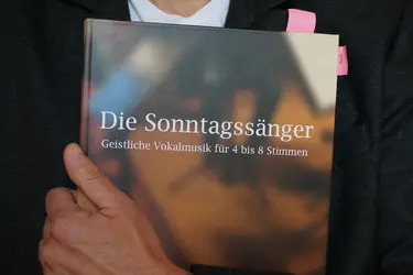 Jemand hält ein dickes Notenbuch vor dem Körper
