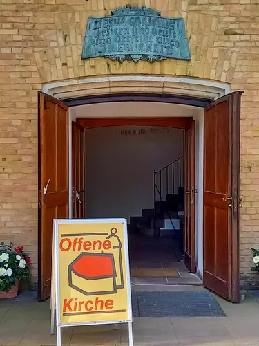Die Türen des Kirchengebäudes sind weit geöffnet. Links davor steht ein Schild, auf dem geschrieben steht "Offene Kirche"