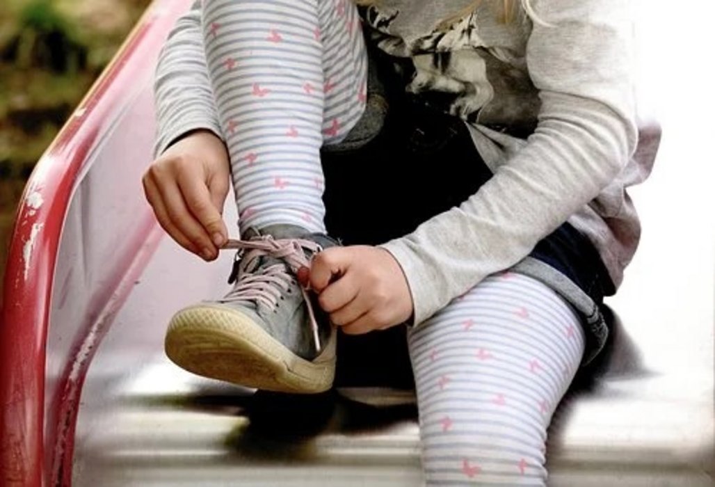 Ein Kind sitzt auf einer Rutsche und bindet sich die Schuhe zu