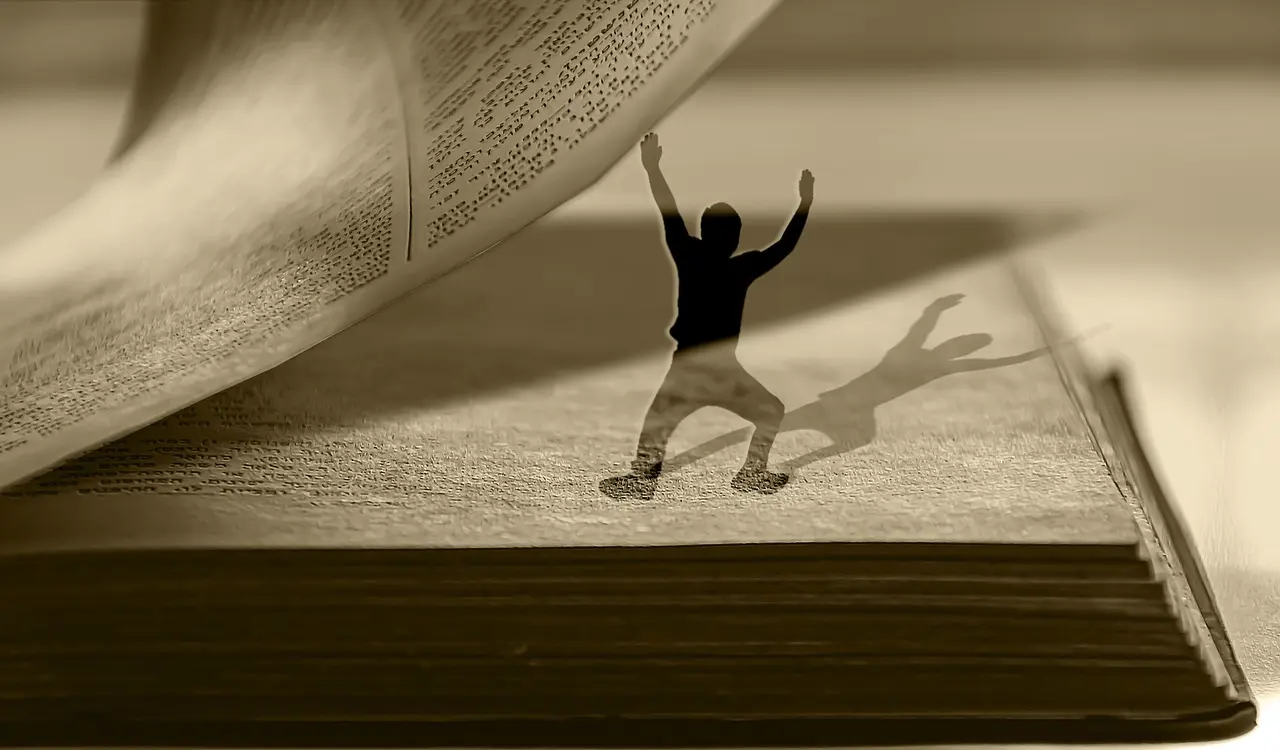Ein Mensch aus Papier steht in einem aufgeschlagenen Buch und stemmt eine Seite nach oben