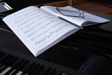 Ein aufgeklapptes Buch mit Noten liegt auf einem Klavier und auf den Noten liegt eine Brille