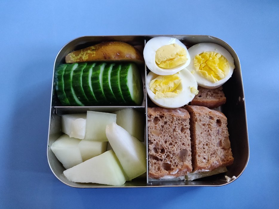 eine Brotdose mit Brot, Eiern, Gurke und anderem Gemüse gefüllt