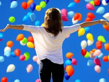 Eine Frau von hinten, die ihre Arme ausstreckt unud in einen Himmel voller Luftballons schaut